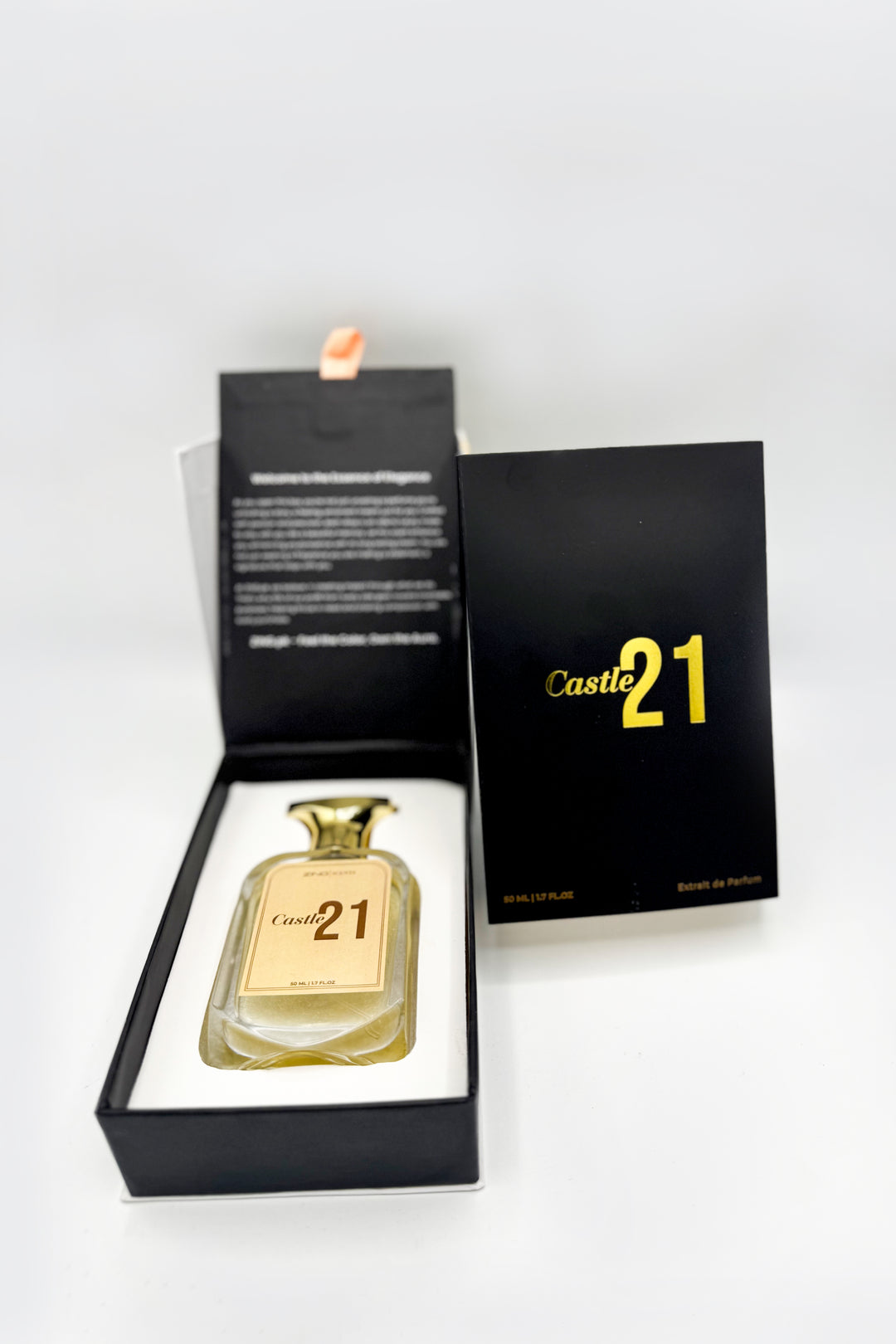 Castle 21 perfume bottle in it's packaging of black box laid on floor in a premium black and white display box next to its minimalist black outer sleeve with gold branding