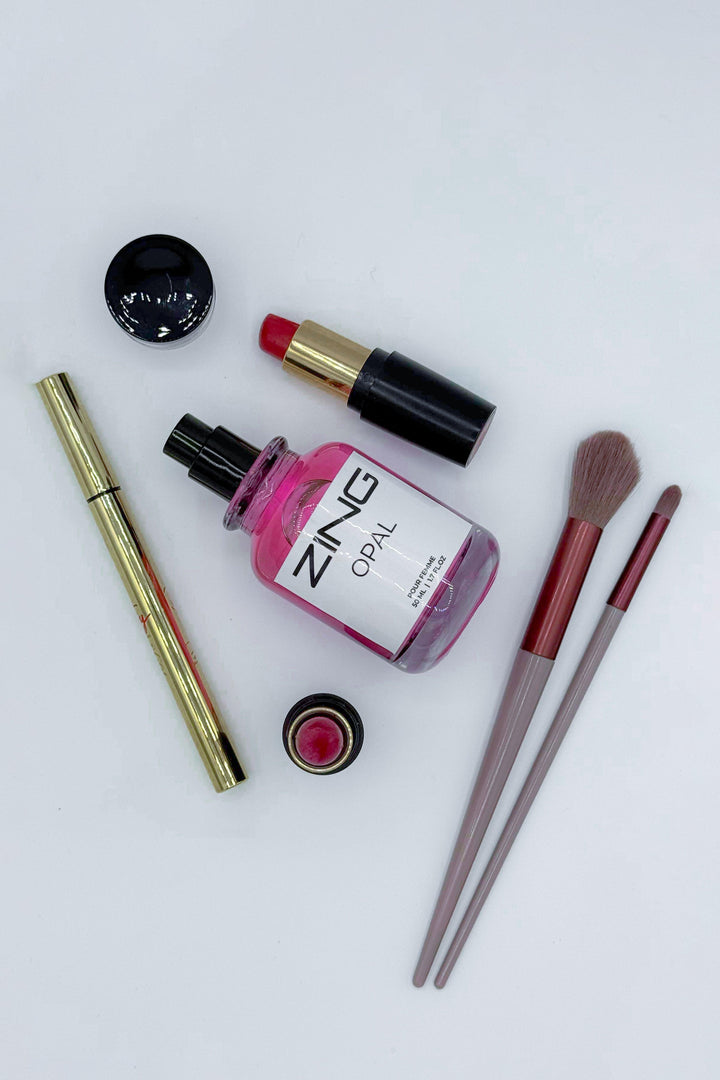Opal perfume bottle laying on white background along with lipstick, eyeliner and makeup brush