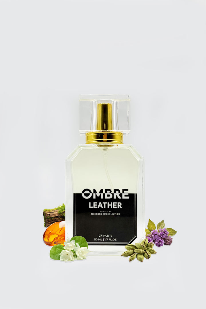 Clear glass perfume bottle labeled Ombre Leather with gold spray cap, placed with leather wood, amber resin, green cardamom, and floral accents on a white background
